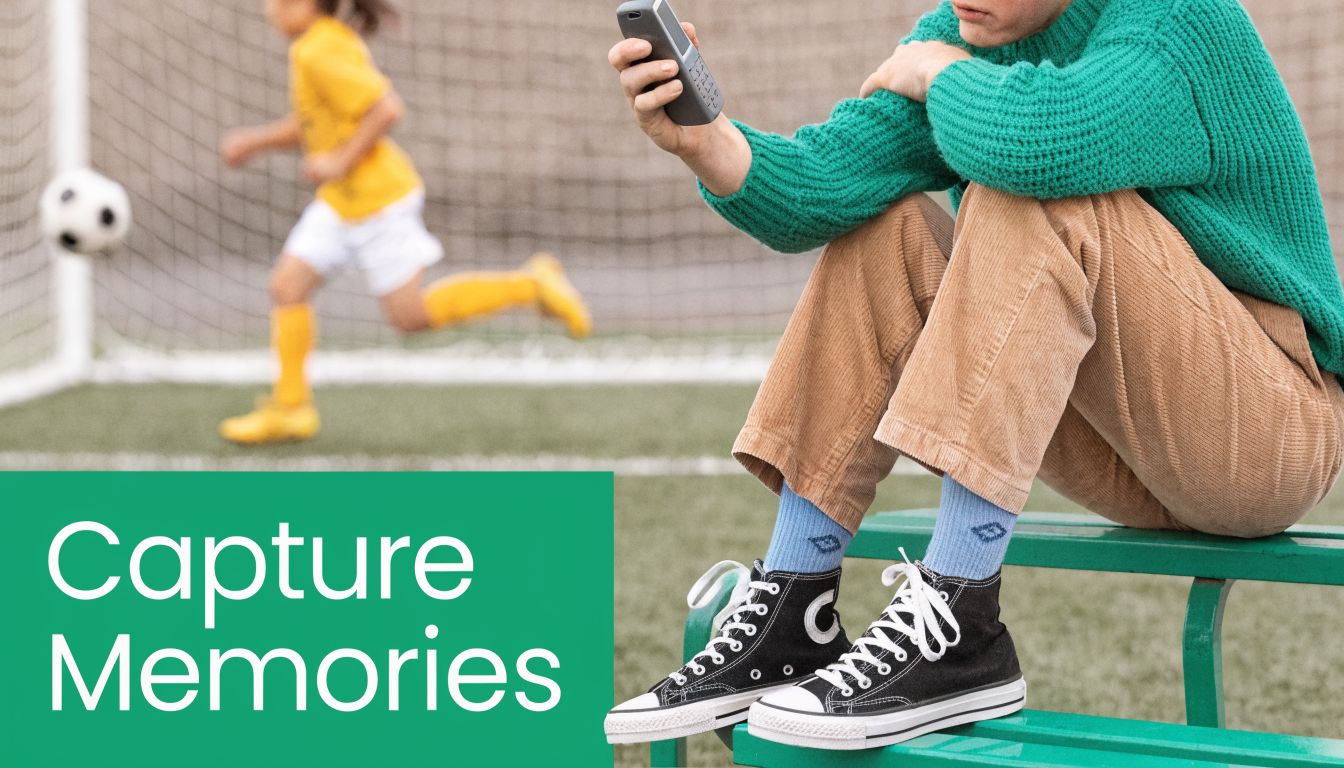 A person sitting on a bench holding a retro cell phone while a child plays soccer nearby.