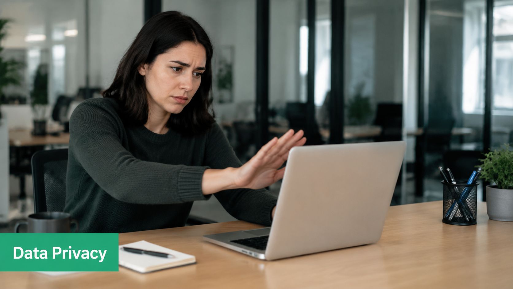 A concerned woman sitting at an office desk signaling stop with her hand towards a laptop.